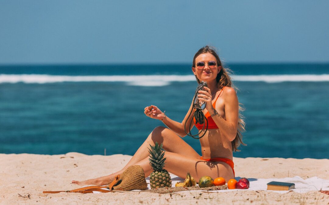 a woman sitting on the beach sand holding a jar