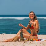 a woman sitting on the beach sand holding a jar